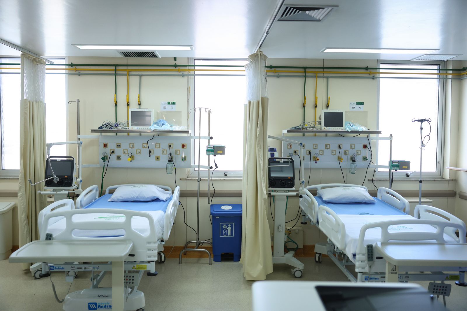 Dois leitos vazios em enfermaria de hospital, com monitores e cortinas