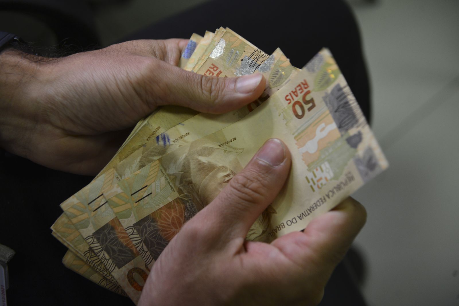 Mãos contam cédulas de cinquenta e de vinte reais