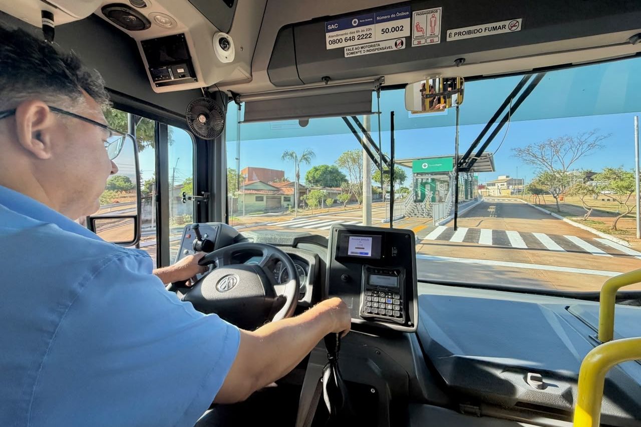 Motorista conduz onibus do transporte coletivo, com estacao de embarque a frente.