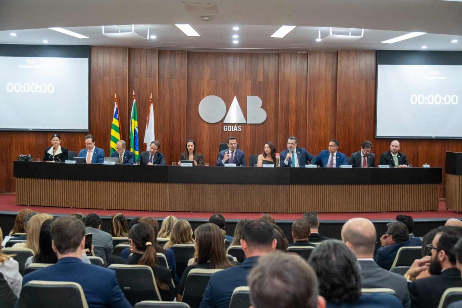 Mesa do Conselho Pleno da OAB-GO durante sessão, diante de plateia de advogados.