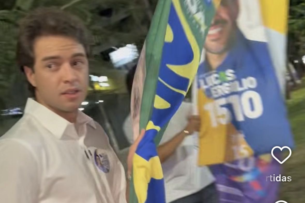 Candidato segura bandeira de campanha a noite em via publica de Goiania, com material de outro candidato ao fundo