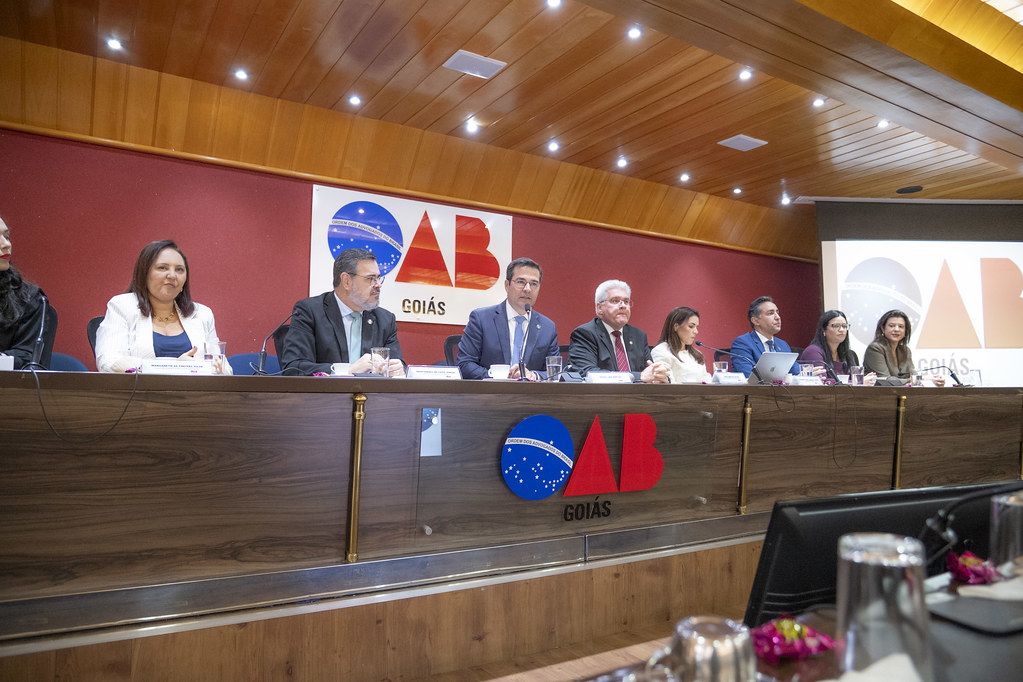 Autoridades sentadas a mesa de sessao no auditorio da OAB Goias, com o logotipo da entidade ao fundo