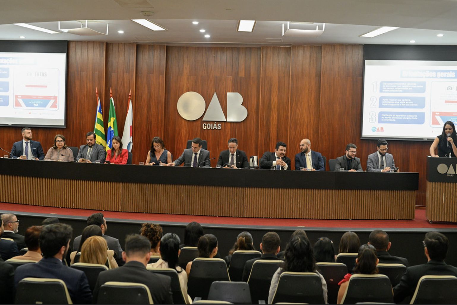 Mesa de autoridades na sala de sessões da sede da OAB-GO, em Goiânia, com o logotipo da Seccional ao fundo e plateia de advogados
