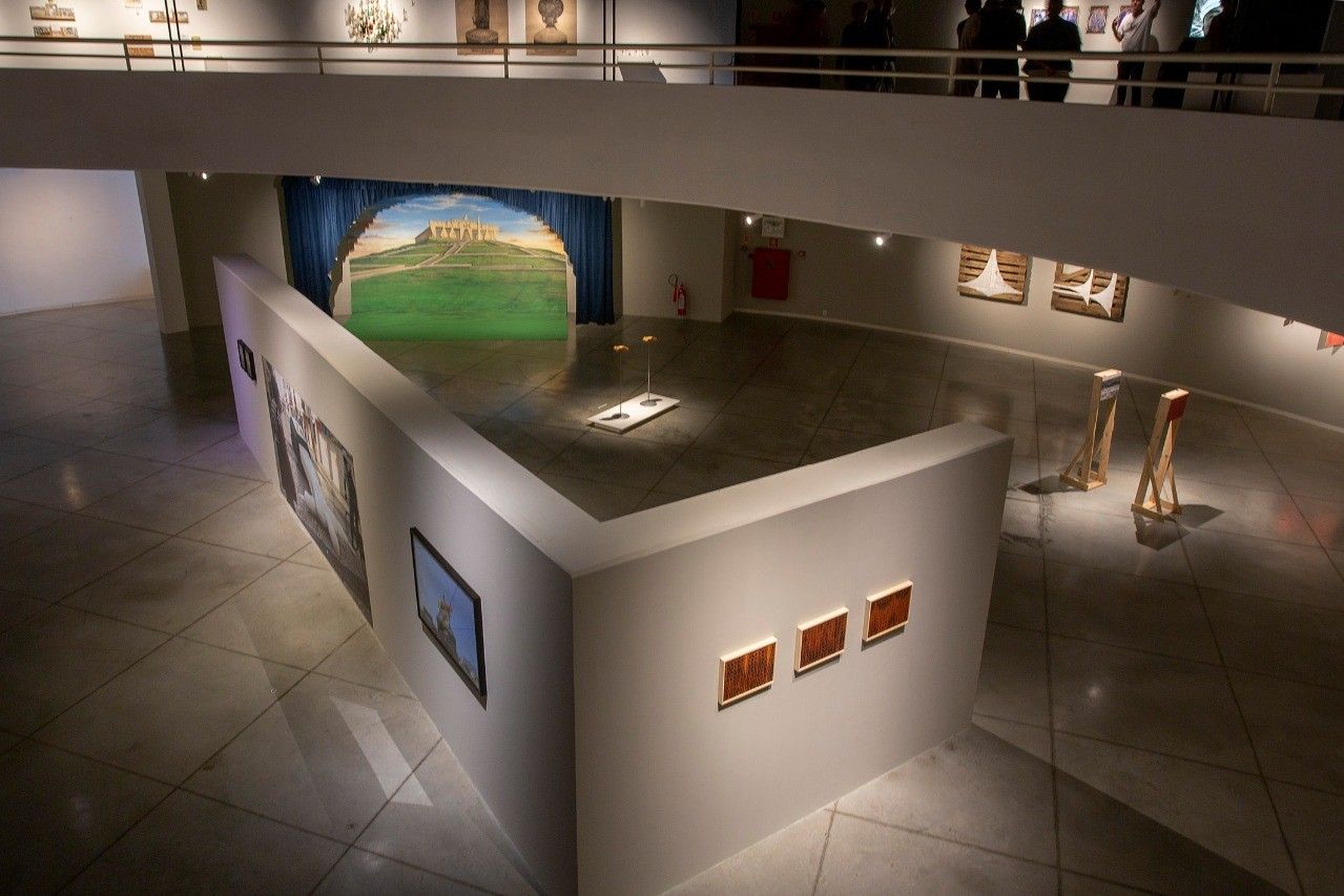 Sala expositiva com paredes brancas, obras de arte contemporânea e mezanino