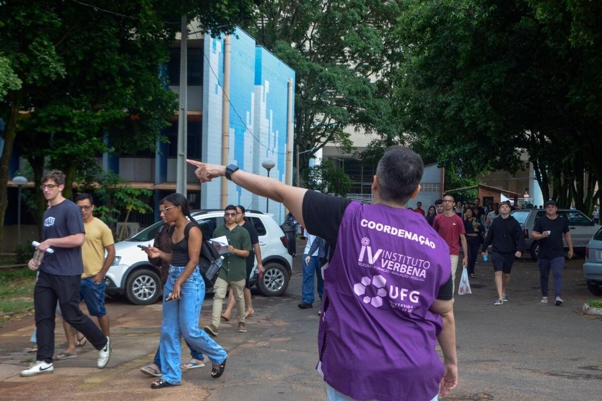 Candidatos caminham até o local de prova enquanto integrante da coordenação do Instituto Verbena/UFG orienta o acesso