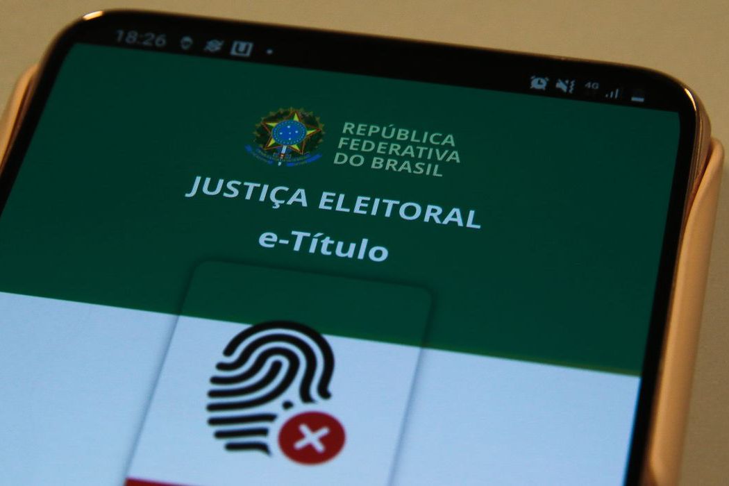 Mão segurando celular com o aplicativo e-Título aberto na tela