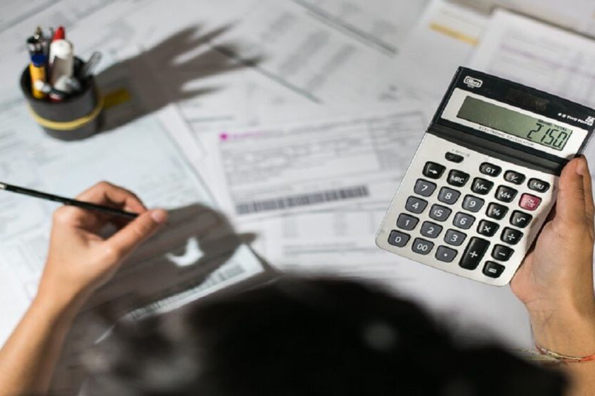 Mão segura calculadora sobre mesa com formulários, documentos e lápis, em cálculo de imposto
