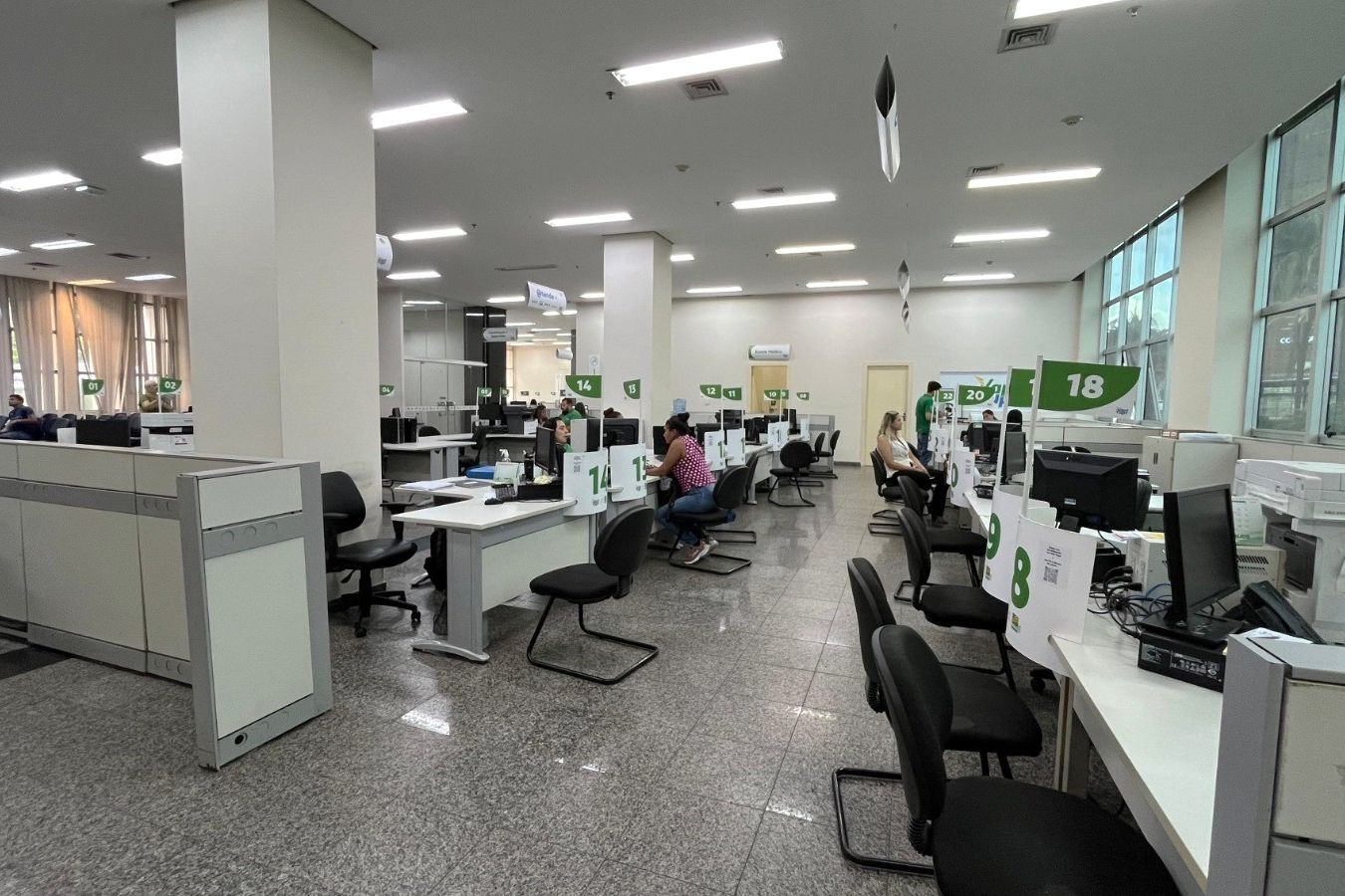 Salão com guichês numerados e computadores em unidade de atendimento ao público