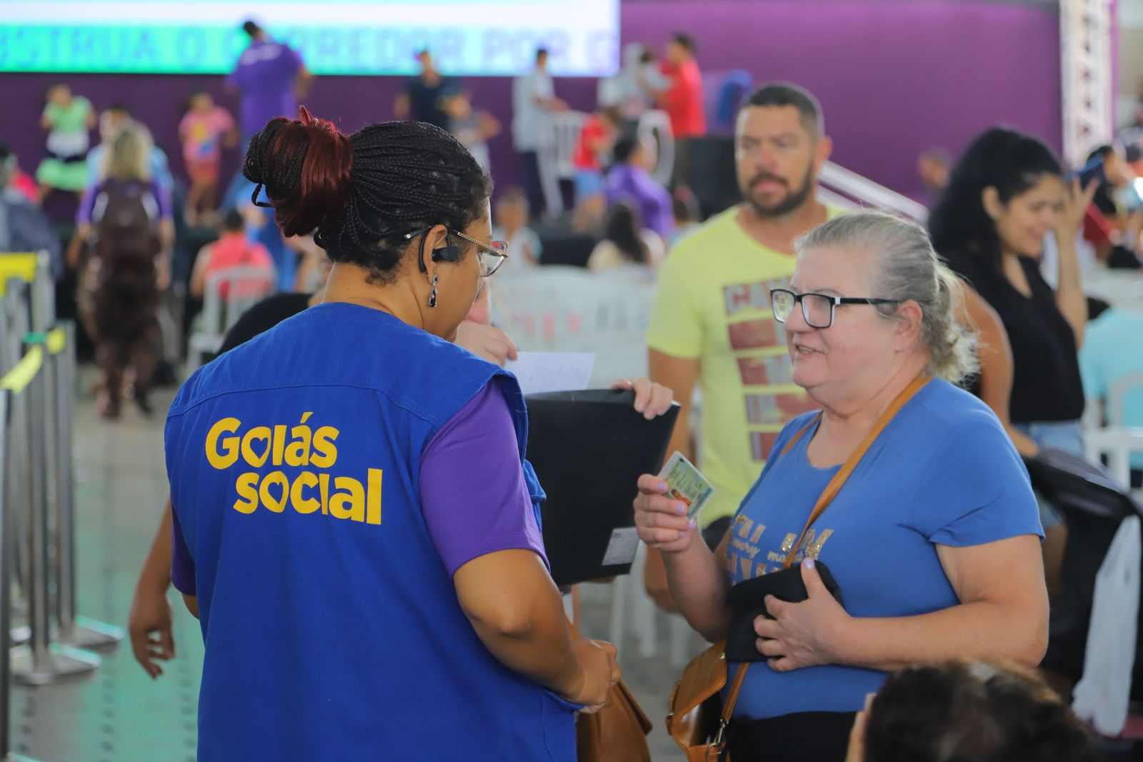 Servidora de colete do Goi&aacute;s Social atende mulheres em fila de entrega de benef&iacute;cios