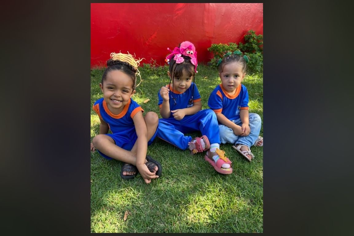 Crianças com uniforme azul sentadas na grama em unidade de educação infantil de Goiânia