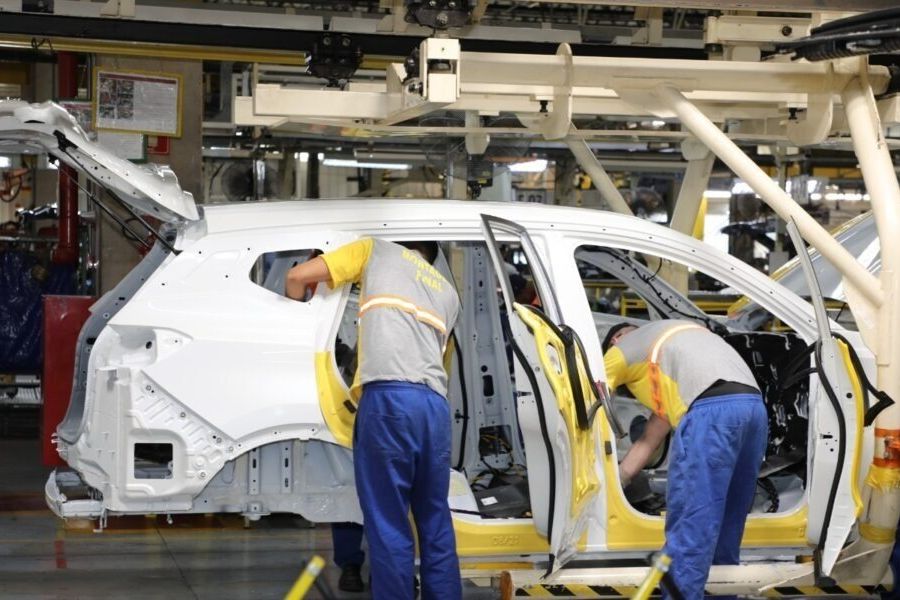 Operários trabalham em carroceria de veículo numa linha de montagem industrial