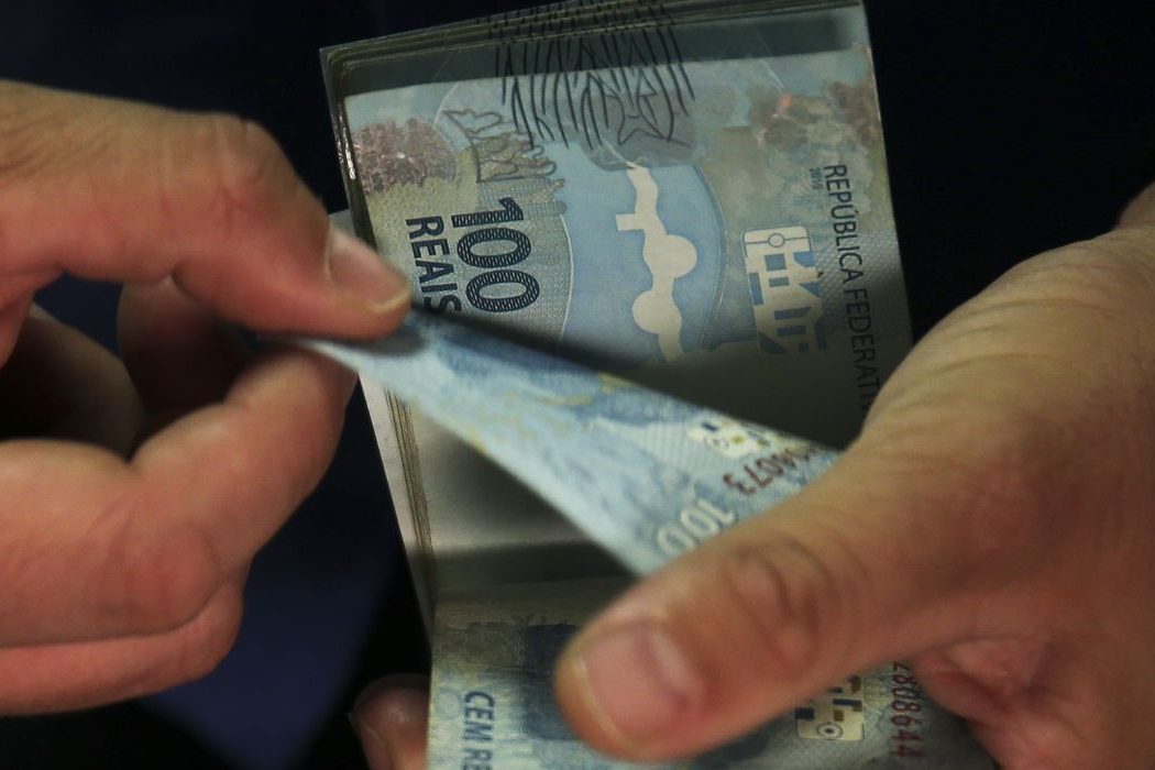 Mãos contando cédulas de cem reais