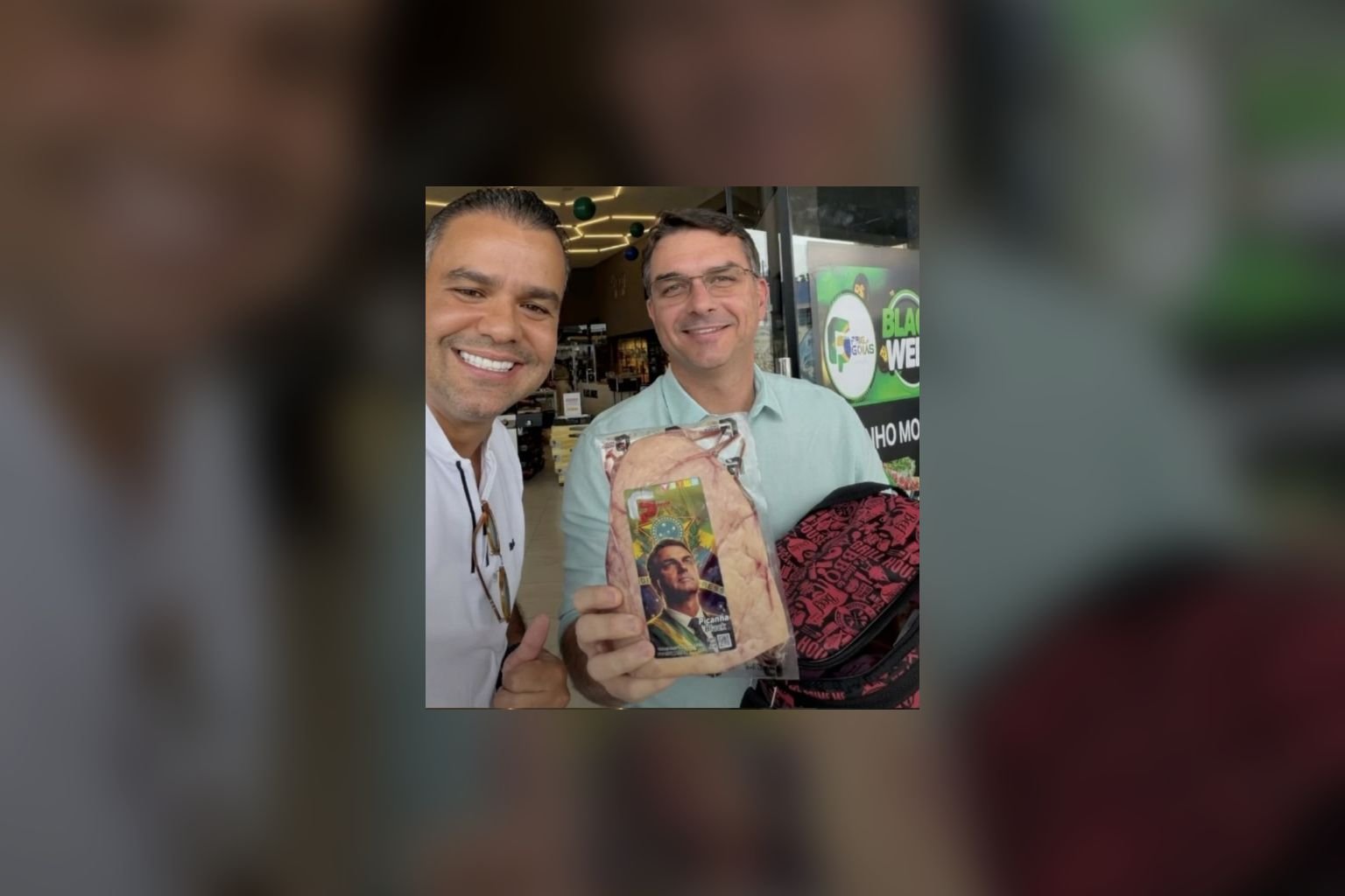Empresário e Flávio Bolsonaro posam com uma peça de picanha embalada em frente a um supermercado