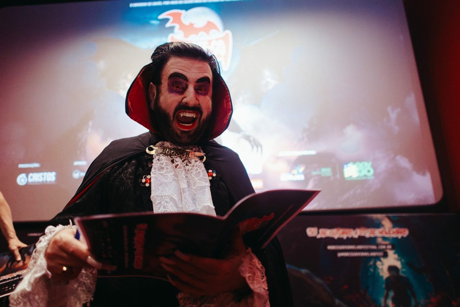 Homem fantasiado de vampiro lê um livreto diante da tela de cinema