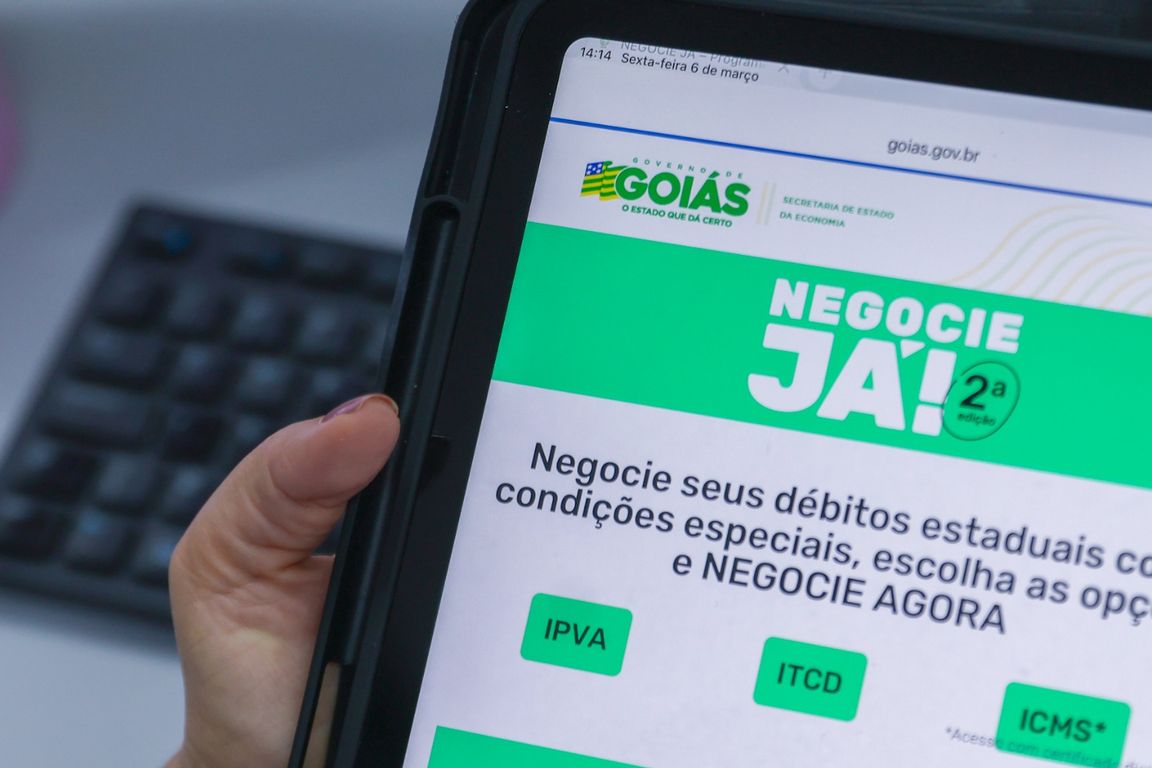 Mãos de uma pessoa usam um tablet com a página do programa Negocie Já II, do Governo de Goiás