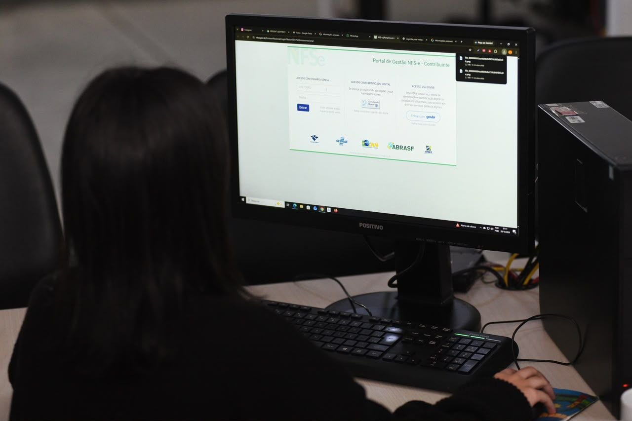 Pessoa de costas usa computador com o portal da nota fiscal de serviço eletrônica aberto na tela
