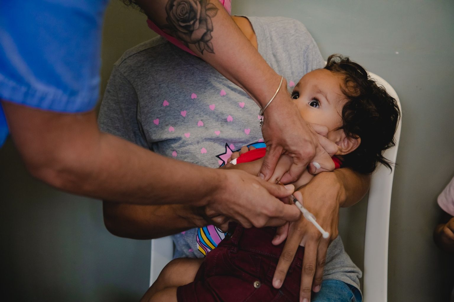 Criança recebe dose de vacina no braço, no colo do responsável