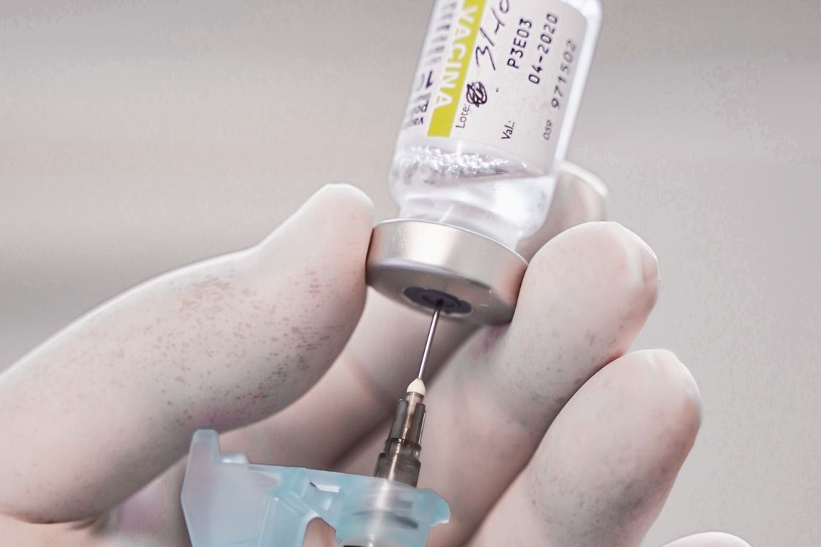 Mãos com luva preparam seringa a partir de frasco de vacina