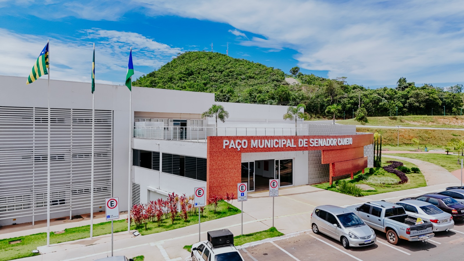 Fachada do Paço Municipal de Senador Canedo, com bandeiras hasteadas e estacionamento à frente