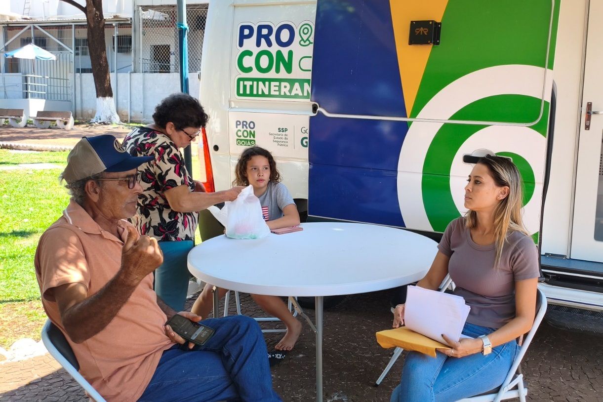 Van do Procon Itinerante com equipe atendendo moradores em mesa ao ar livre