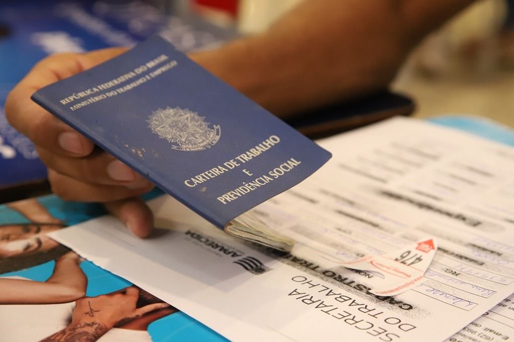 Mão segura carteira de trabalho sobre formulários de cadastro de vagas de emprego