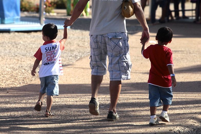 Adulto caminha de mãos dadas com duas crianças
