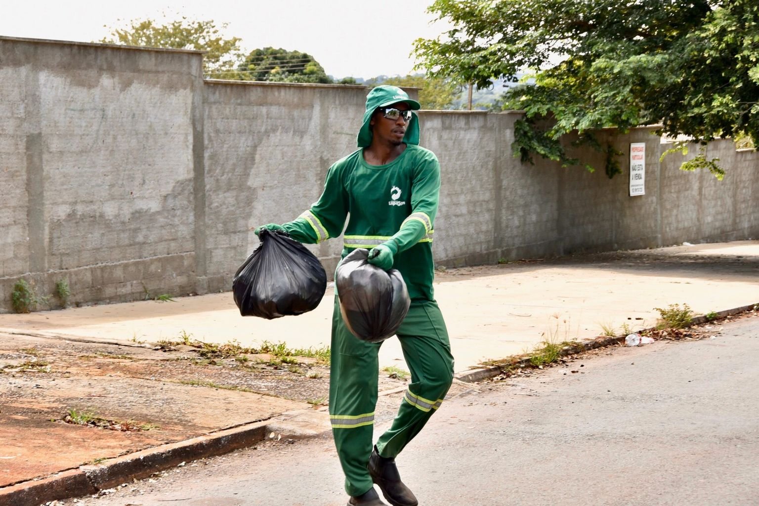 Gari de uniforme verde carrega sacos de lixo em rua de Goiânia