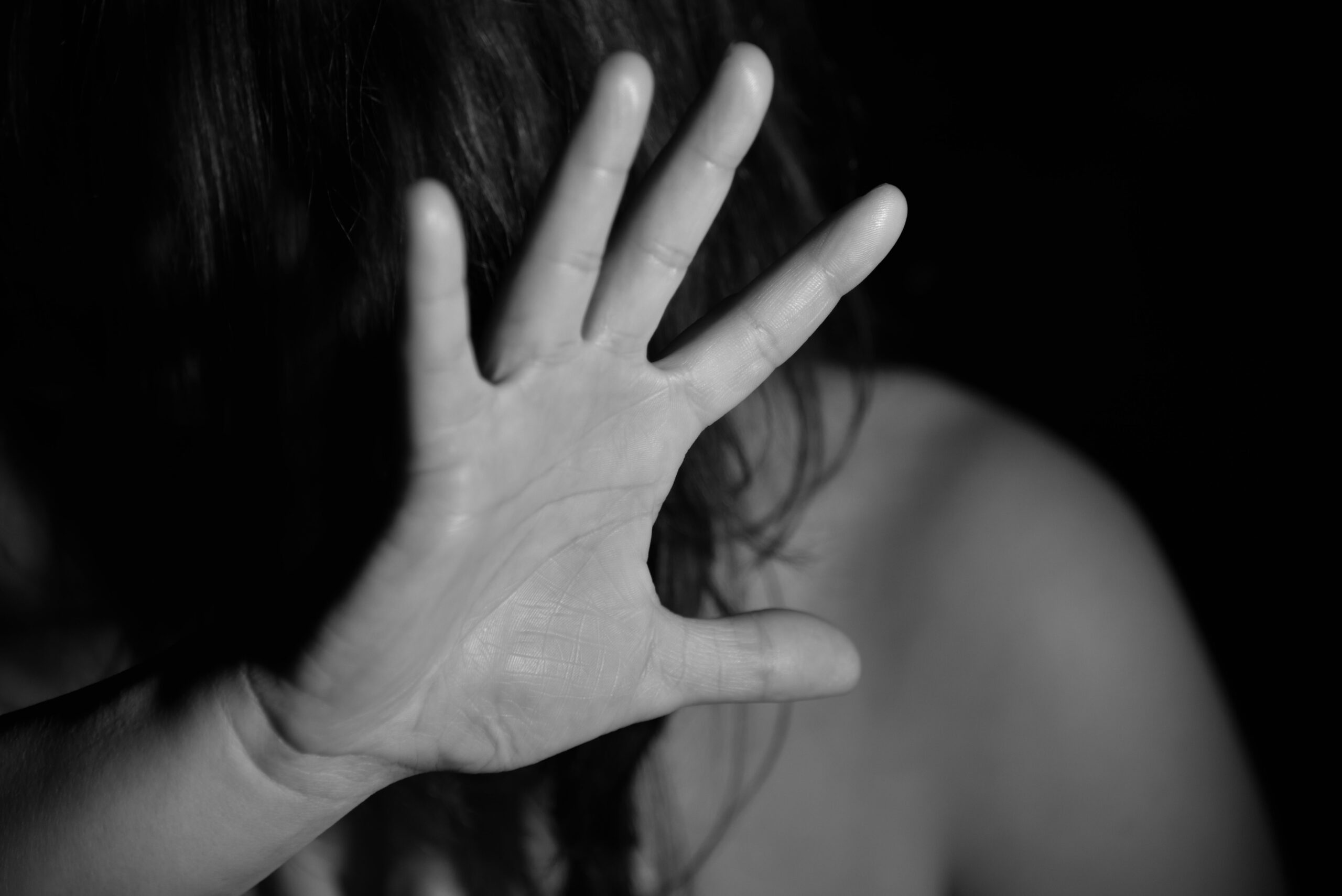 Mulher de costas estende a mão aberta em gesto de defesa, em foto em preto e branco